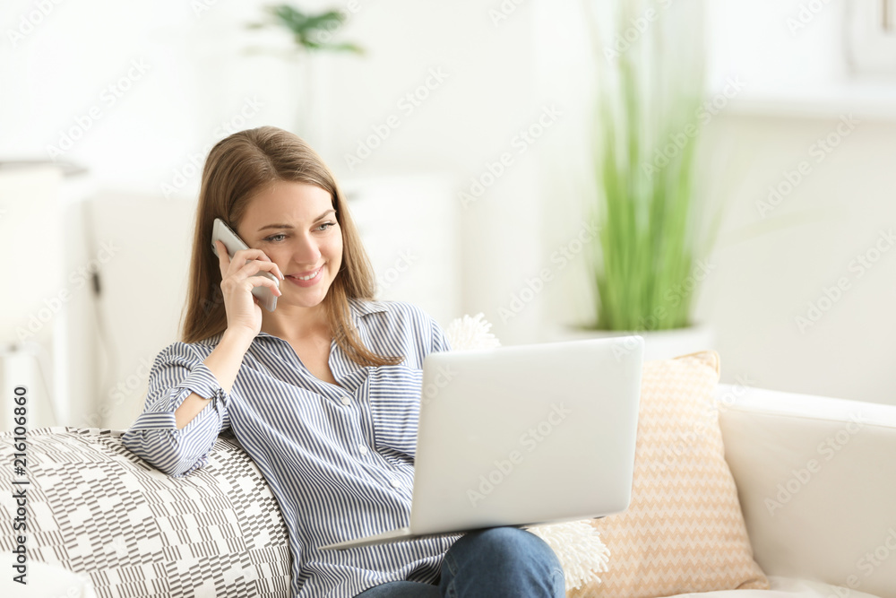 Female freelancer talking by phone while working on laptop at home Female freelancer talking by phone while working on laptop at home