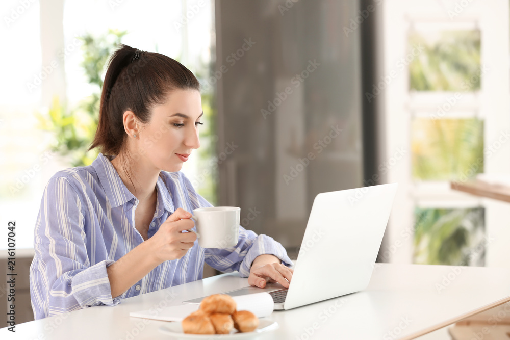 Young female freelancer drinking coffee while working with laptop at home Young female freelancer drinking coffee while working with laptop at home