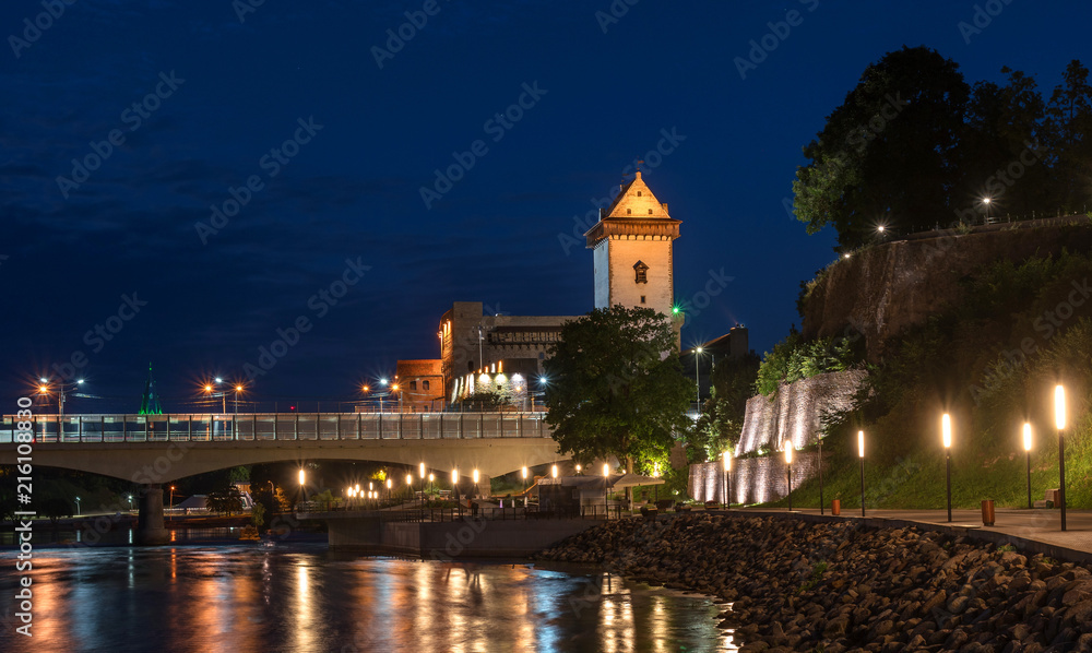 Night panorama of the Narva castle with the tower High Herman, Narva, Estonia. In the foreground is the city promenade and a bridge across the Narova River. The bridge connects Estonia and Russia