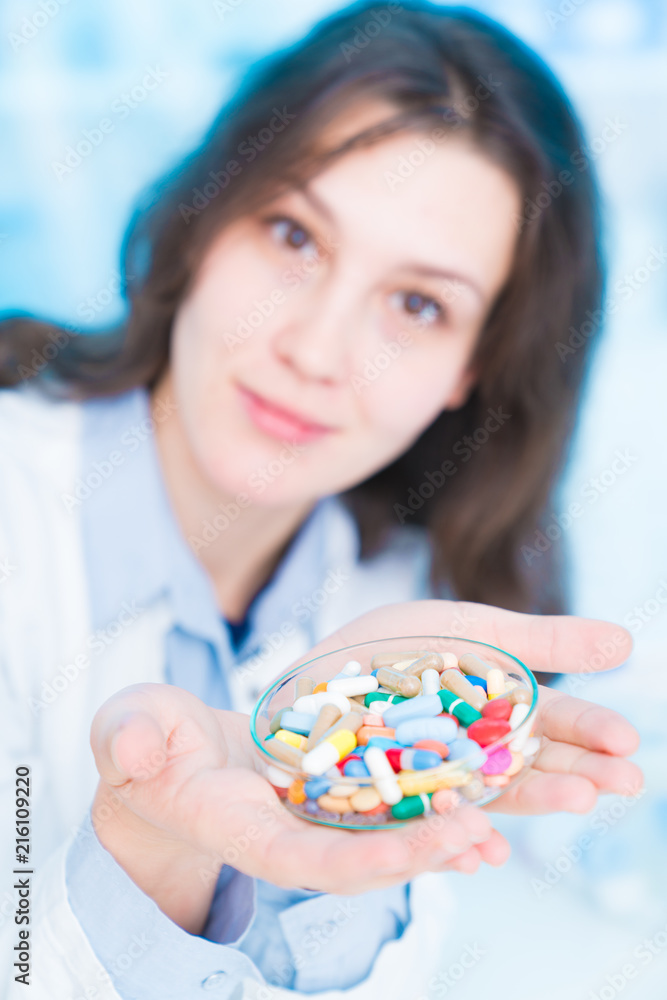 young woman doctor smiling and holding one pill over blue background young woman doctor smiling and holding one pill over blue background