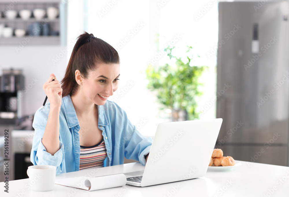 Happy female freelancer with laptop in kitchen Happy female freelancer with laptop in kitchen