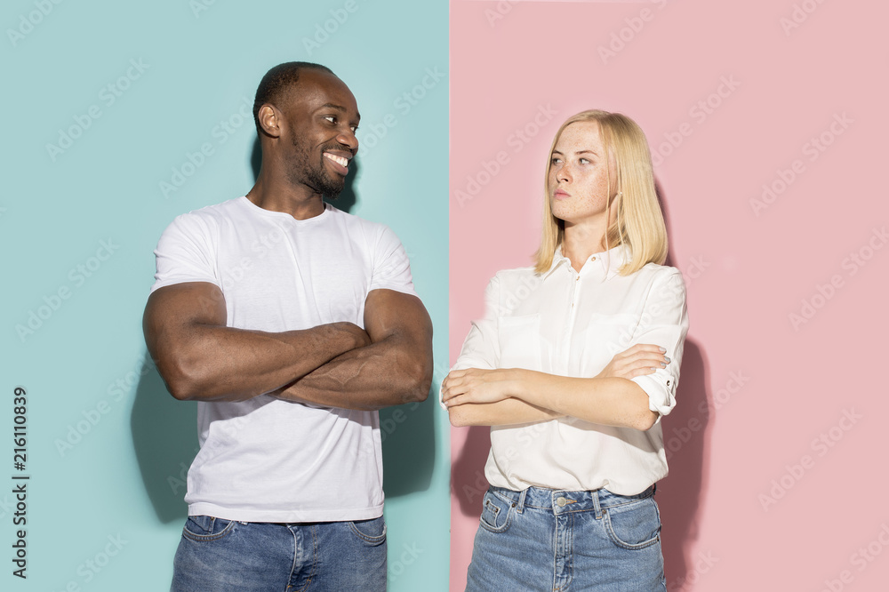 Closeup portrait of young couple, man, woman. One being excited happy smiling, other serious, concerned, unhappy on pink and blue background. Emotion contrasts Closeup portrait of young couple, man, woman. One being excited happy smiling, other serious, concerned, unhappy on pink and blue background. Emotion contrasts