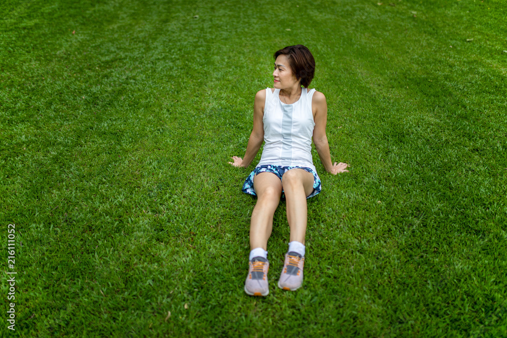 Asian woman wearing sportwear sitting on grass field with smile face and relaxed posture Asian woman wearing sportwear sitting on grass field with smile face and relaxed posture