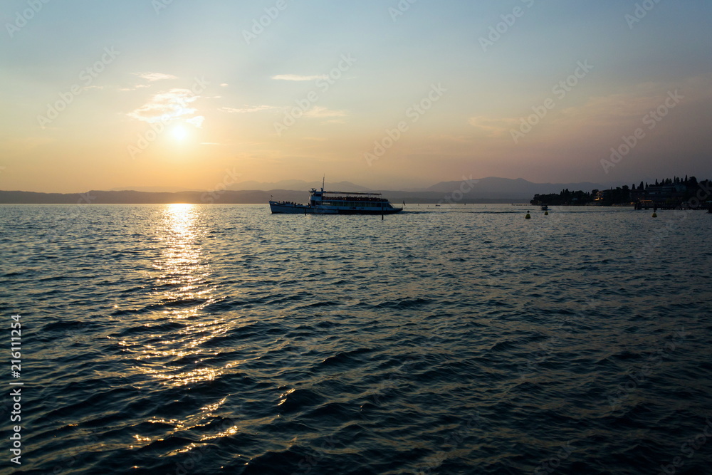 Ferry floating on Lago di Garda near Scaliger Castle during beautiful sunset, Sirmione, Italy