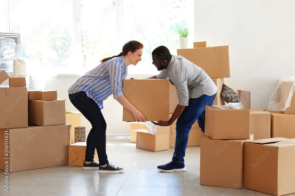 Interracial couple carrying box indoors. Moving into new house Interracial couple carrying box indoors. Moving into new house