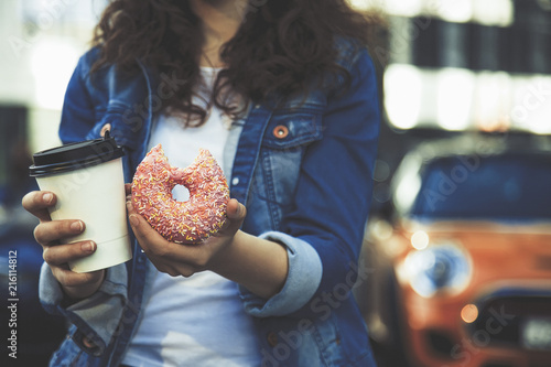 hands holding a cup of coffee and pink donut in street