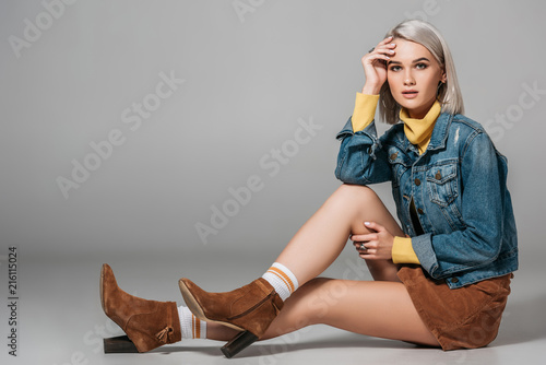 beautiful model in trendy corduroy skirt and jeans jacket sitting on floor, on grey