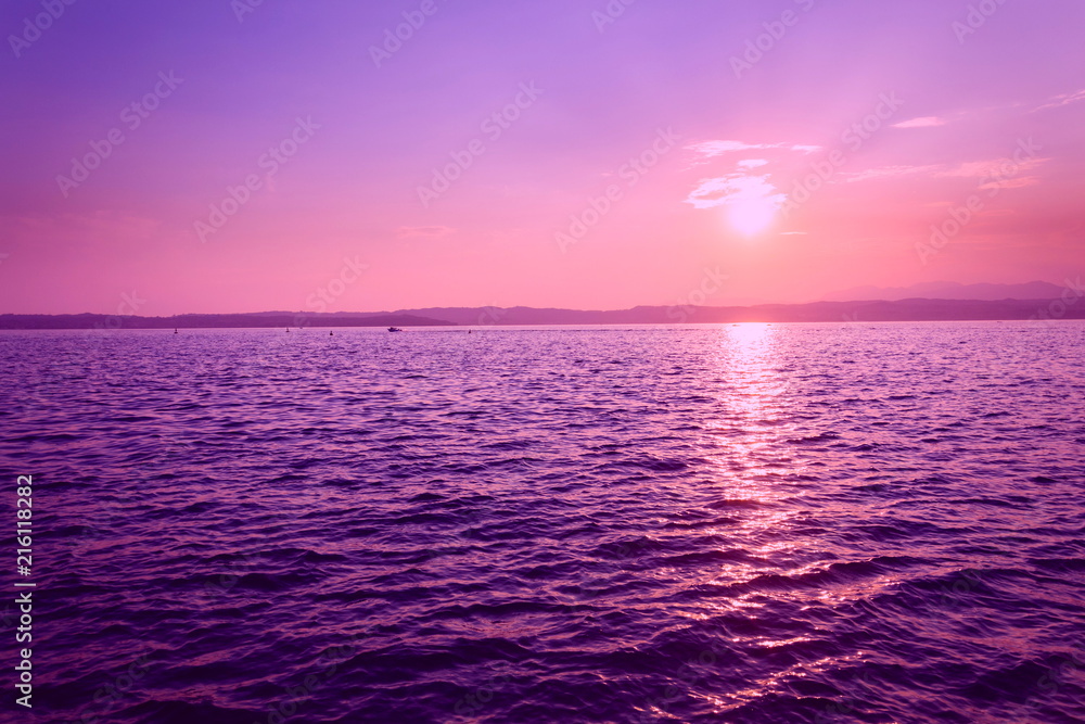 Obraz premium Beautiful purple sunset with floating boat on Lago di Garda near Scaliger Castle, Sirmione, Italy, romantic love concept