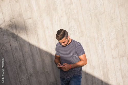 young caucasian teenager man use the phone to connect with friends and check emails and social media on internet. light and shadow composition in the urban city. wall background