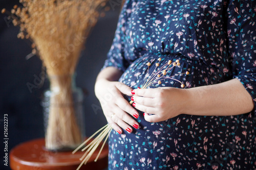 Closeup of pregnant woman holding flower and touching her belly