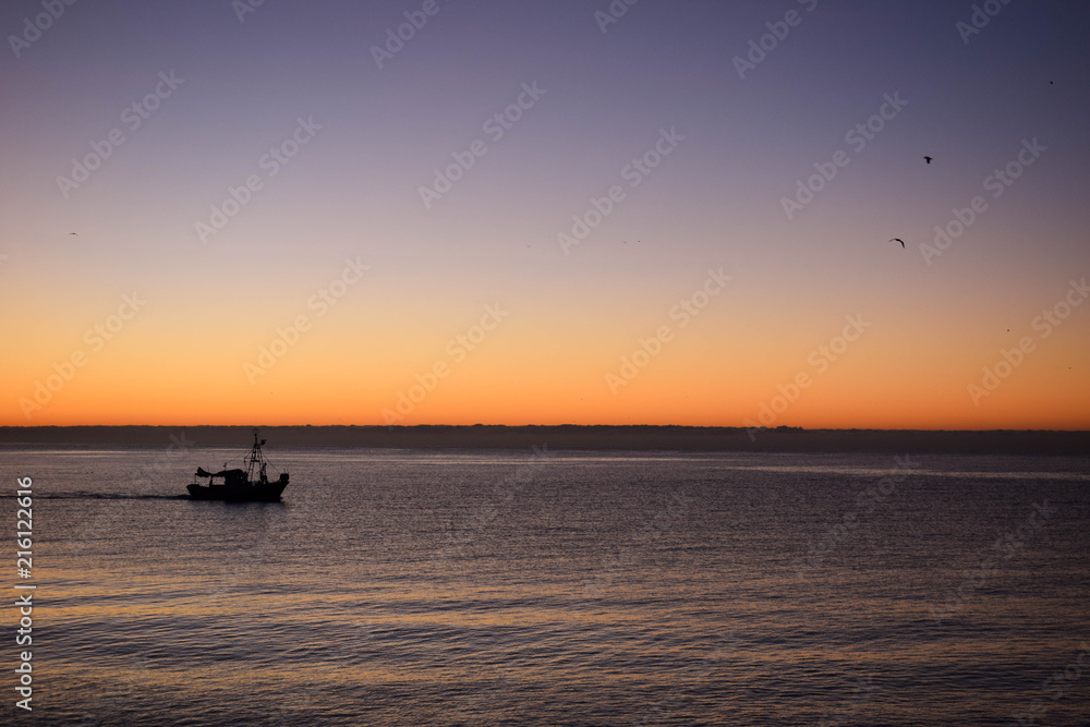 Sunrise over the sea with the silhouette of a boat.