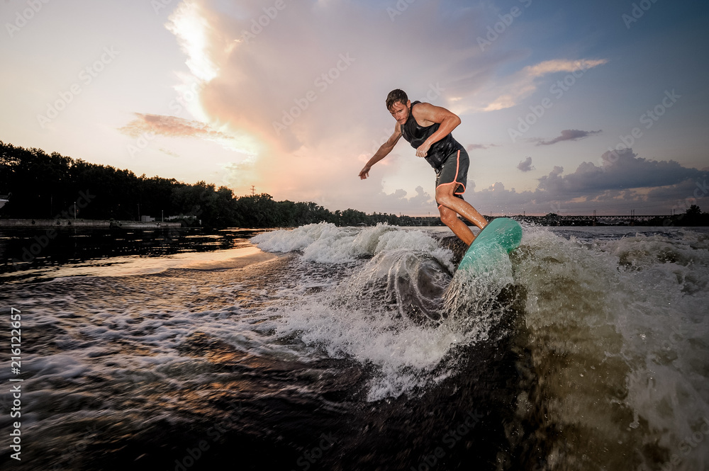 Young wakesurfer riding on river waves in the evening