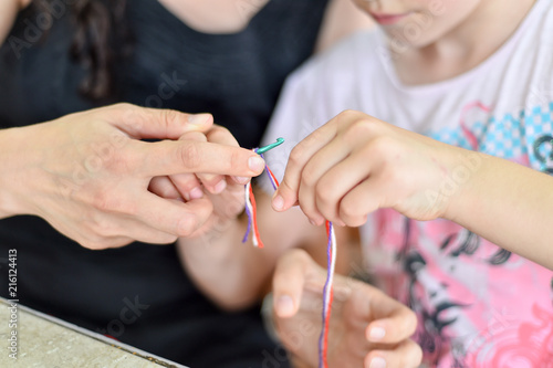 Hands of an adult and hands of a child knitting together