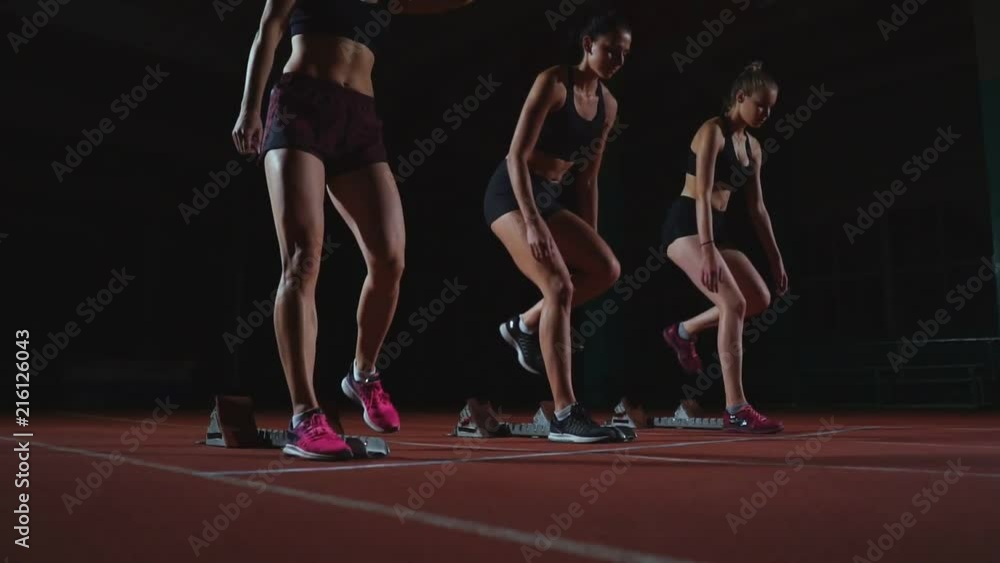 Female runners at athletics track crouching at the starting blocks before a race. In slow motion. Female runners at athletics track crouching at the starting blocks before a race. In slow motion.