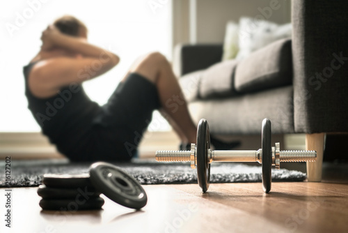 Home workout. Man doing ab training and crunches in living room gym. Guy doing sit ups. Warm up before weight exercise. Fitness concept with dumbbell and athlete.