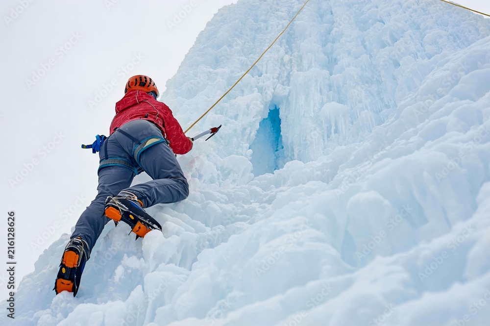 Alpinist woman with ice tools axe in orange helmet climbing a l Alpinist woman with ice tools axe in orange helmet climbing a l