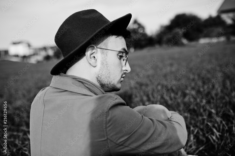 Stylish man in glasses, brown jacket and hat with bag posed on green field. Stylish man in glasses, brown jacket and hat with bag posed on green field.