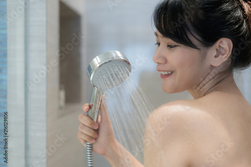 Young Asian woman taking a shower in the bathroom with Shower head. Looking happy and relax.