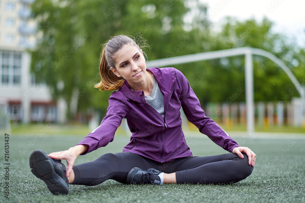 Fit woman stretching her leg to warm up. On football field