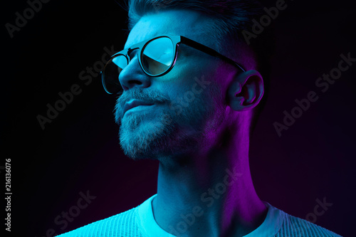 Neon light studio close-up portrait of serious man model with mustaches and beard in sunglasses and white t-shirt