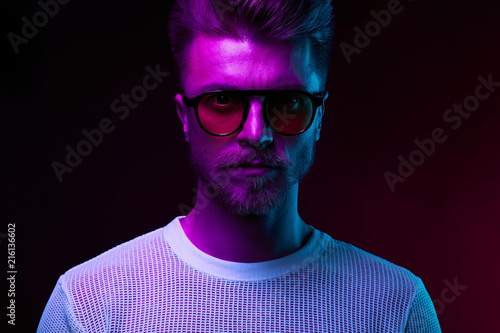 Neon light portrait of serious man model with mustaches and beard in sunglasses and white t-shirt © monchak