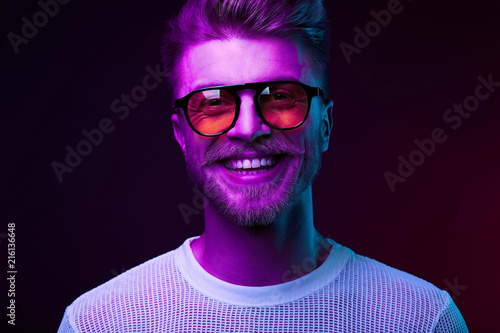 Neon light portrait of smiling man model with mustaches and beard in orange sunglasses and white t-shirt