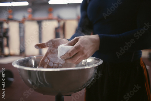 Sportsman applying magnesia on hands in gym, closeup