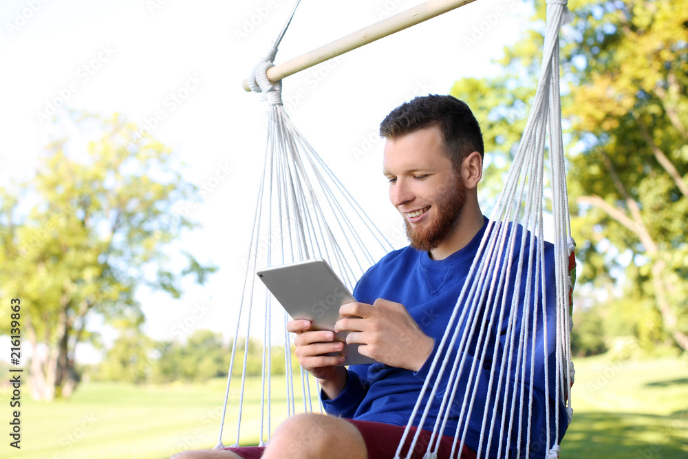 Young man with tablet computer resting in hammock outdoors Young man with tablet computer resting in hammock outdoors