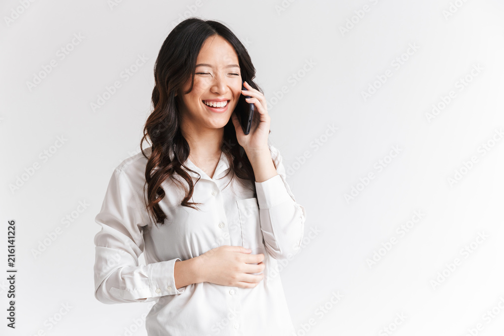 Image of brunette chinese woman with long dark hair holding and talking on cell phone, isolated over white background in studio Image of brunette chinese woman with long dark hair holding and talking on cell phone, isolated over white background in studio