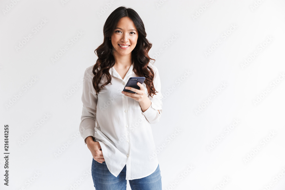 Photo of smiling charming asian woman with long dark hair holding black cell phone, isolated over white background in studio Photo of smiling charming asian woman with long dark hair holding black cell phone, isolated over white background in studio