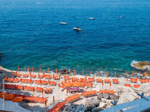 Beach with sunbeds at Praiano cliffs in the Amalfi coast, Italy.