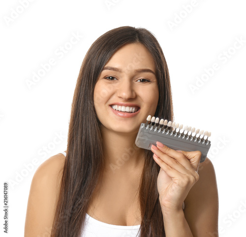 Beautiful young woman with teeth color samples on white background