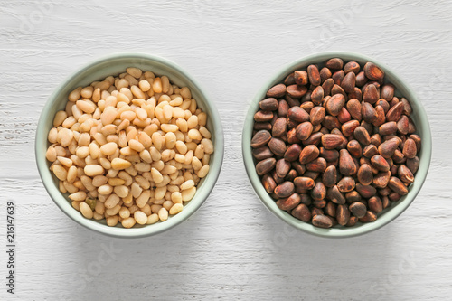 Bowls with tasty pine nuts on white wooden background photo