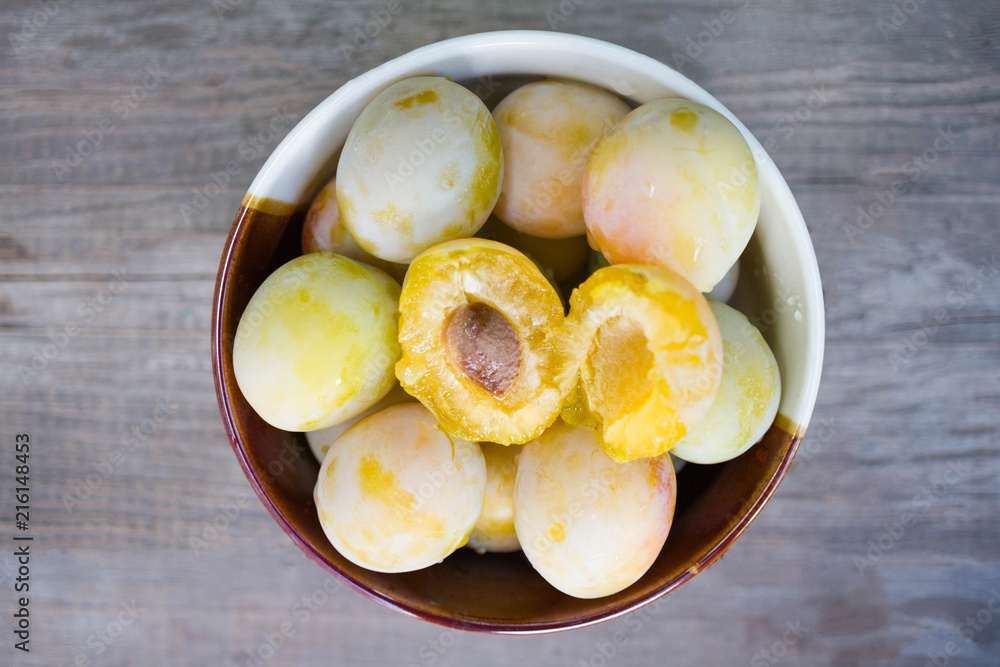 Ripe white plums in a clay bowl on a wooden table. Summer seasonal fruit concept