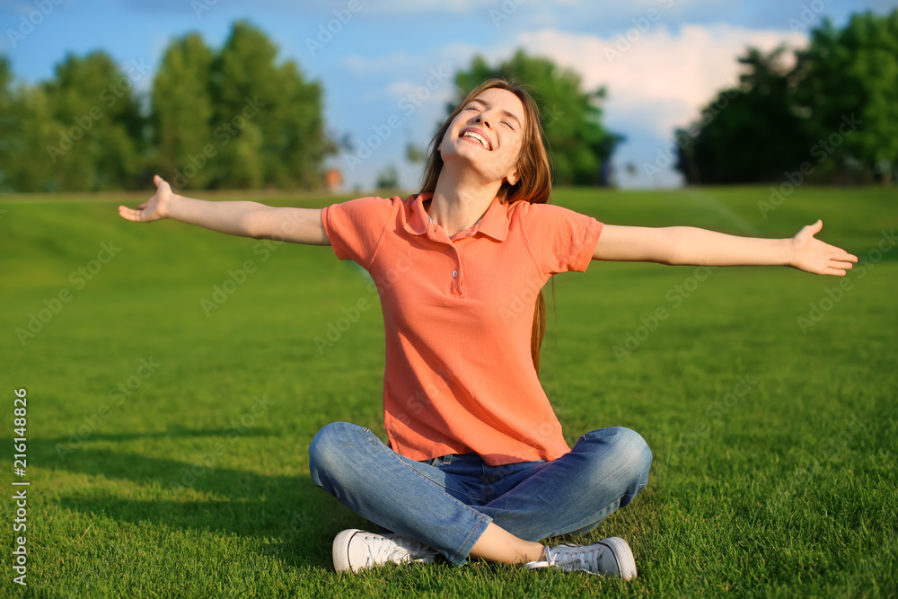 Happy young woman sitting on green grass outdoors Happy young woman sitting on green grass outdoors