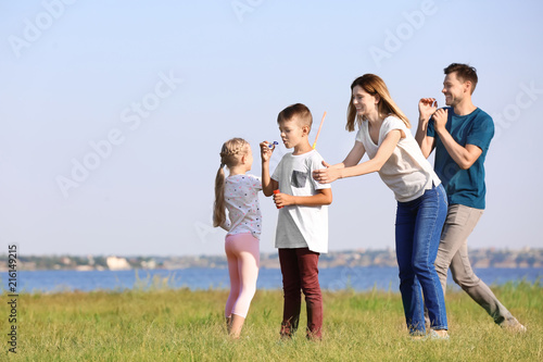 Family blowing soap bubbles near river on summer day