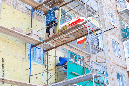 Workers warm and repair the facade of the building. The old house is compacted with mineral wool and the exterior of the building is lined. Work at height without insurance © ALEXEY