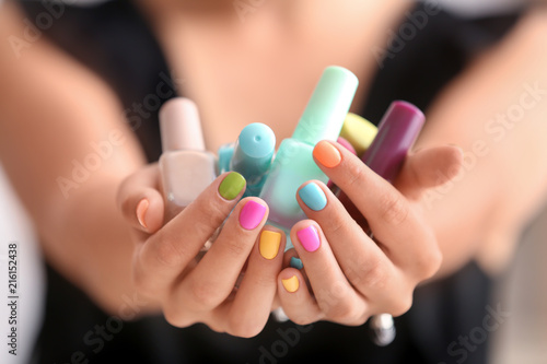 Young woman with colorful manicure holding bottles of nail polishes  closeup