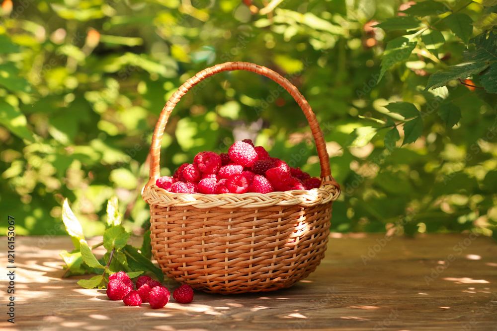 Wicker basket with fresh raspberries on wooden table outdoors Wicker basket with fresh raspberries on wooden table outdoors