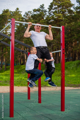 family, father and sons involved in sports on the bar outdoor. Father and sons during street workout in outdoor gym. Strong man and little boys