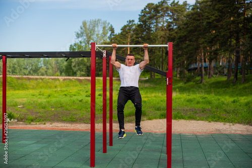 Muscular man doing pull-ups on horizontal bar outdoors. Strong athlete doing pull-up on horizontal bar.