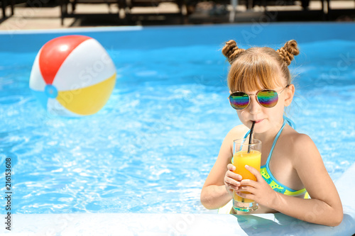 Cute little girl drinking juice in swimming pool