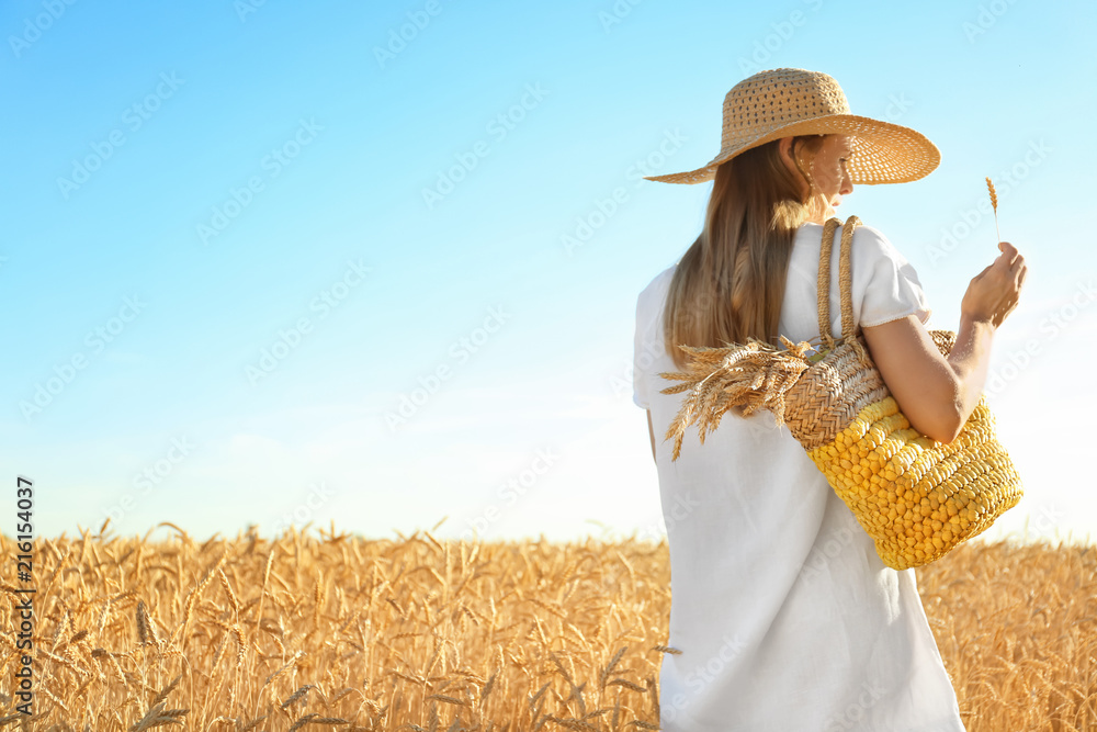 Obraz premium Beautiful woman with wicker bag in wheat field on sunny day