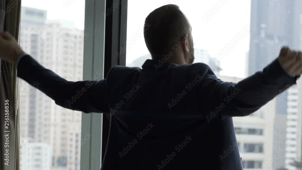 Businessman standing in his apartment in front of the window and stretching muscles
Businessman standing in his apartment in front of the window and stretching muscles