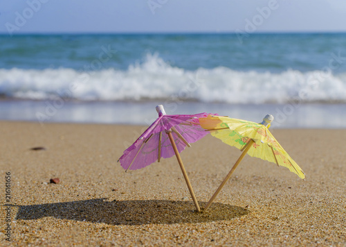 umbrella from a cocktail in female hands on a beach background on a sunny day