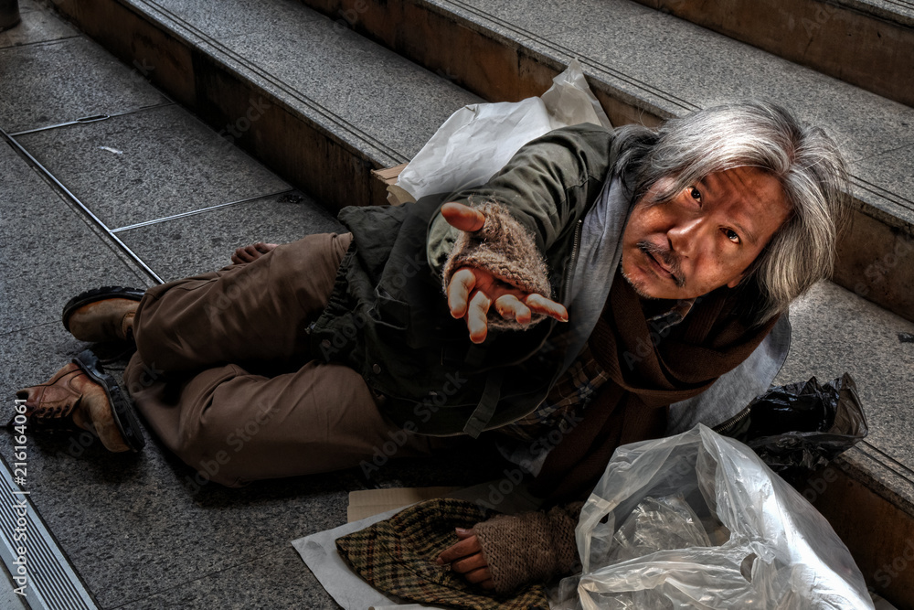 Homeless male showing hand asking for food or money while laying on walk path frool Homeless male showing hand asking for food or money while laying on walk path frool