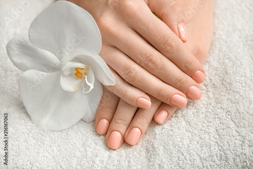 Hands of woman with beautiful manicure and orchid flower on towel, closeup