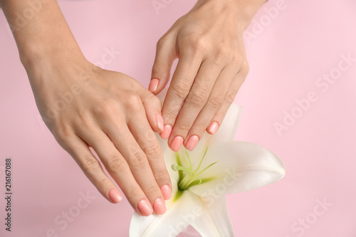 Hands of beautiful young woman with professional manicure and flower on color background