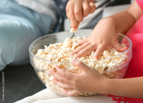 Little children eating popcorn while watching TV on sofa, closeup