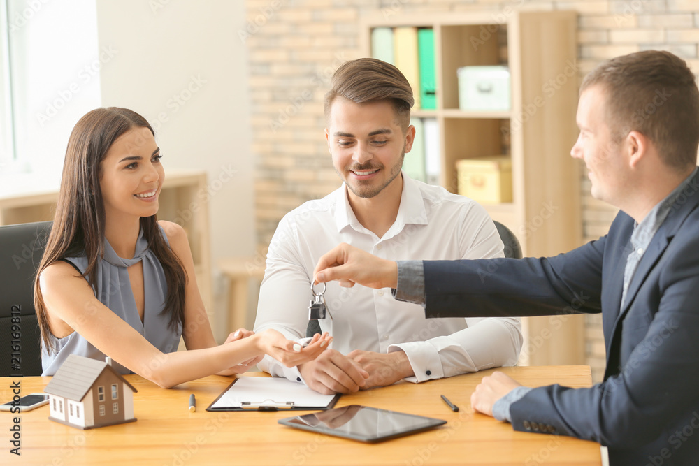 Real estate agent giving key of new house to young couple in office Real estate agent giving key of new house to young couple in office